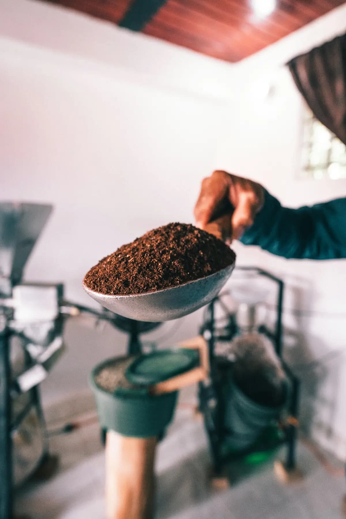 Mano que sostiene un cuenco con café recién molido junto a una tostadora.